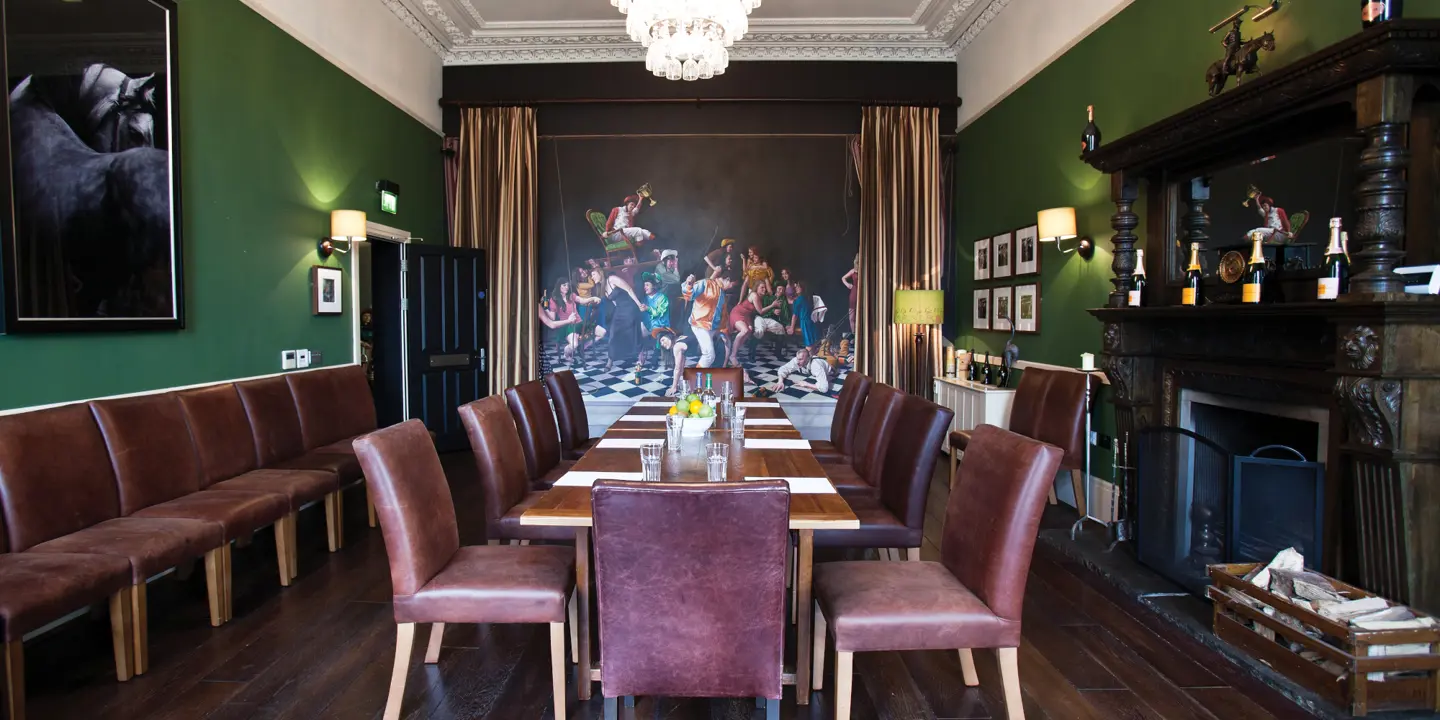 A long wooden table adorned with a bowl of fresh fruit. There are extra chairs in the room