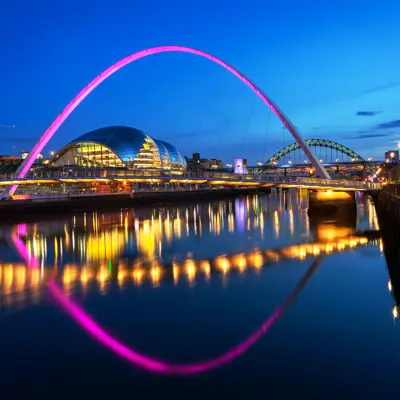 Night time view of the illuminated Millennium Bridge with The Glasshouse International Centre for Music in the background