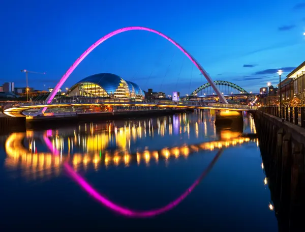 Night time view of the illuminated Millennium Bridge with The Glasshouse International Centre for Music in the background