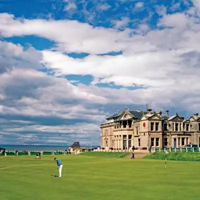 A man playing golf in front of a large old building.