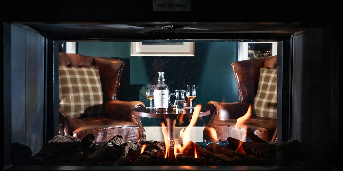 Two chairs and a glass of wine beside a cozy fireplace.