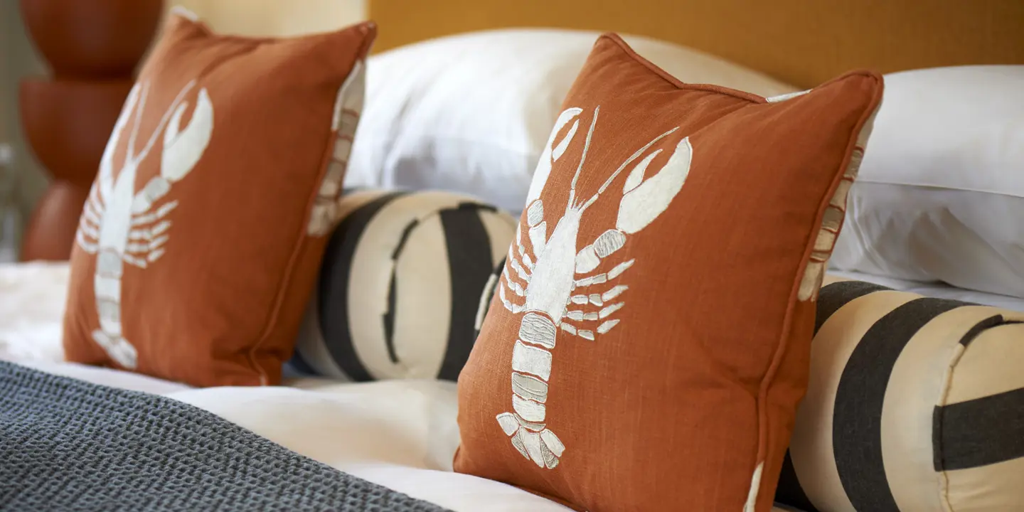 Close-up of pillows with a lobster emblem on a bed.