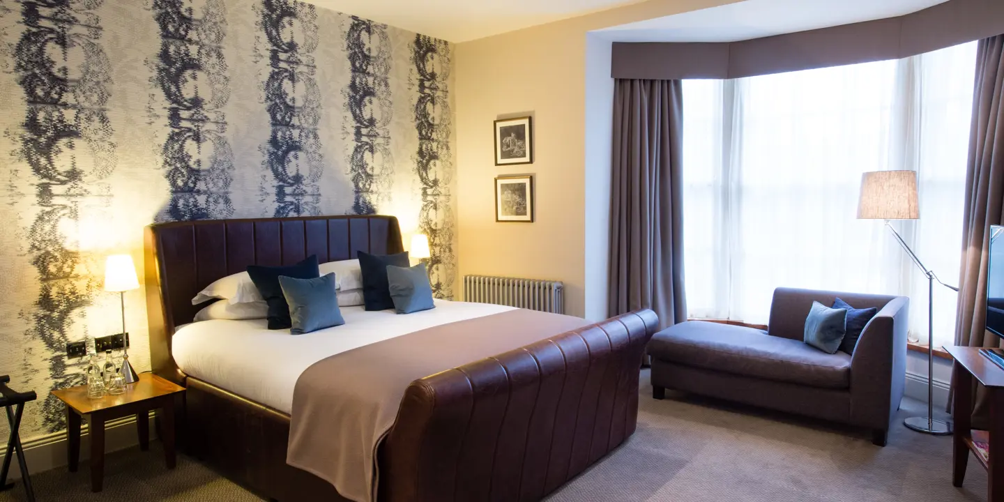 Elegantly made brown leather bed, with plump pillows and 2 framed pictures on the wall