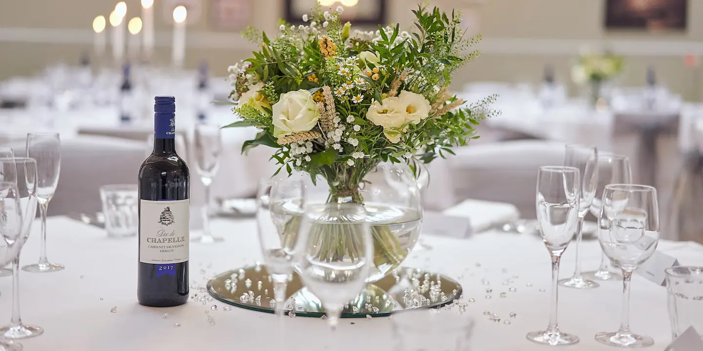 A table displaying a vase filled with flowers and a bottle of wine.