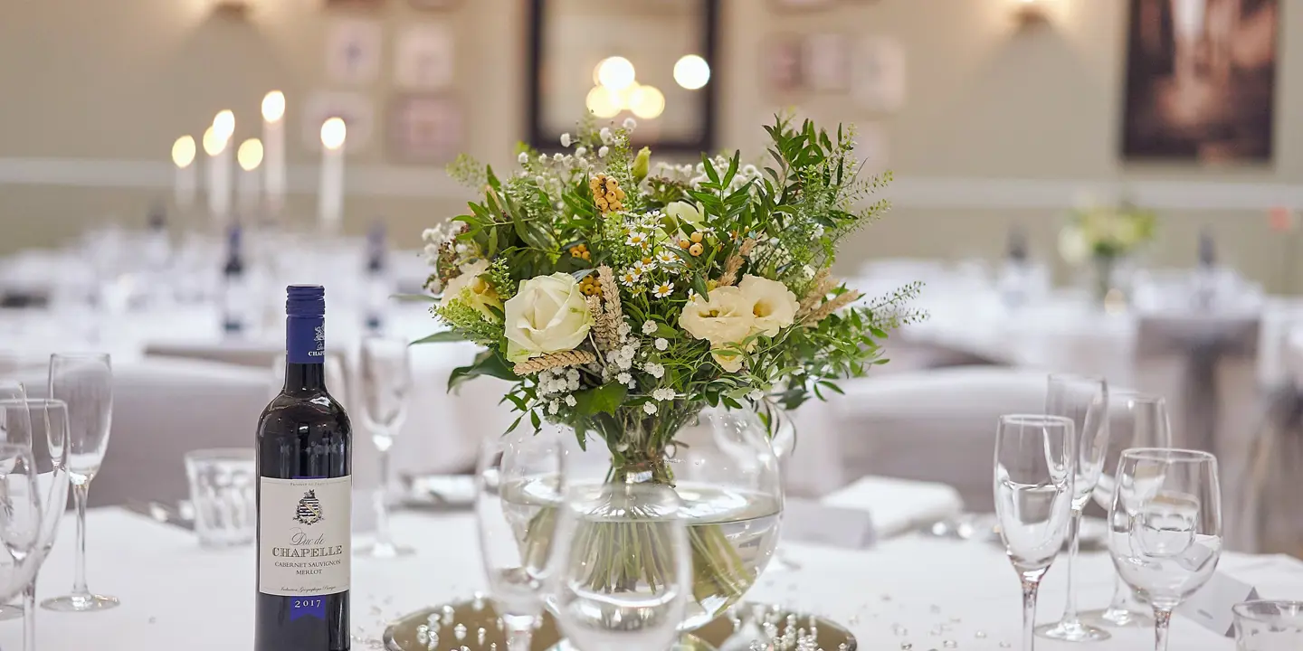 A table displaying a vase filled with flowers and a bottle of wine.