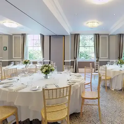 A spacious room adorned with neatly arranged round tables, chairs, and pristine white tablecloths.