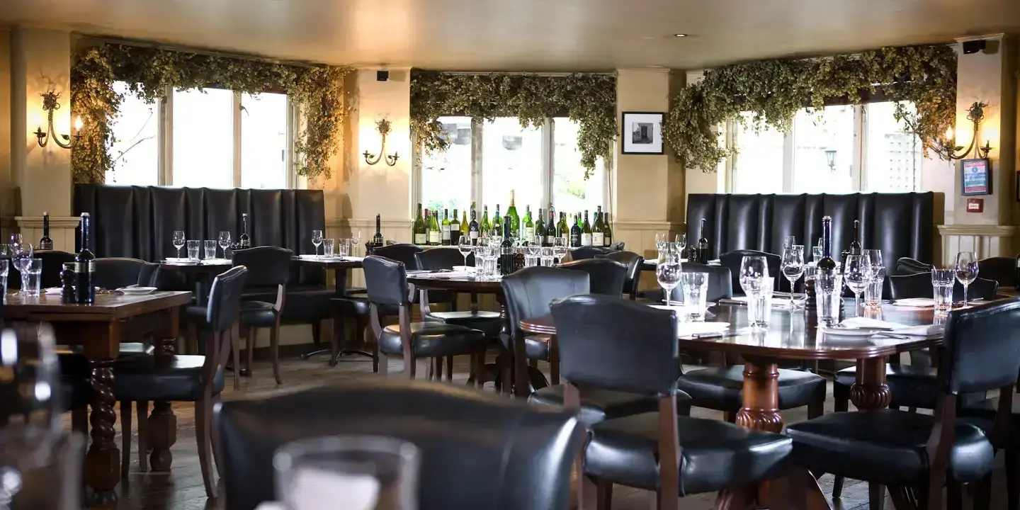 An arrange of wooden tables and black wooden chairs laid out with empty glasses