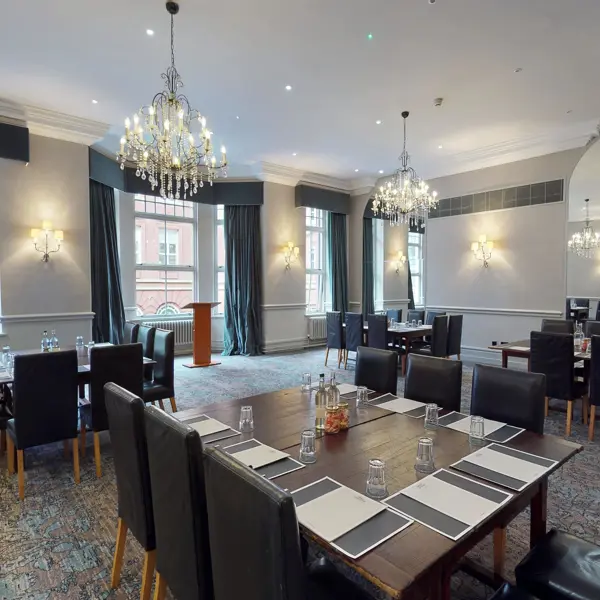 A selection of tables and chairs in a meeting room with 2 elegant chandeliers.