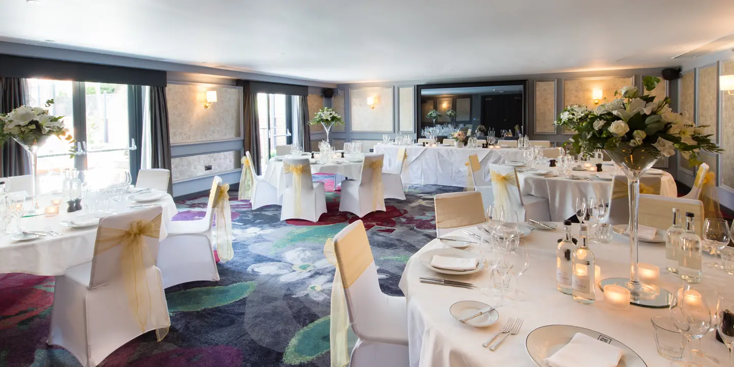 An elegantly decorated banquet room featuring pristine white tables and chairs.