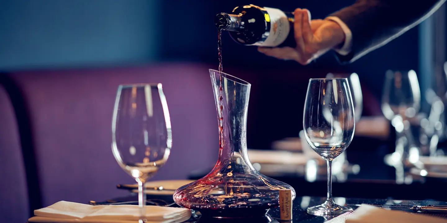 A person pouring wine into a decanter placed on a table.